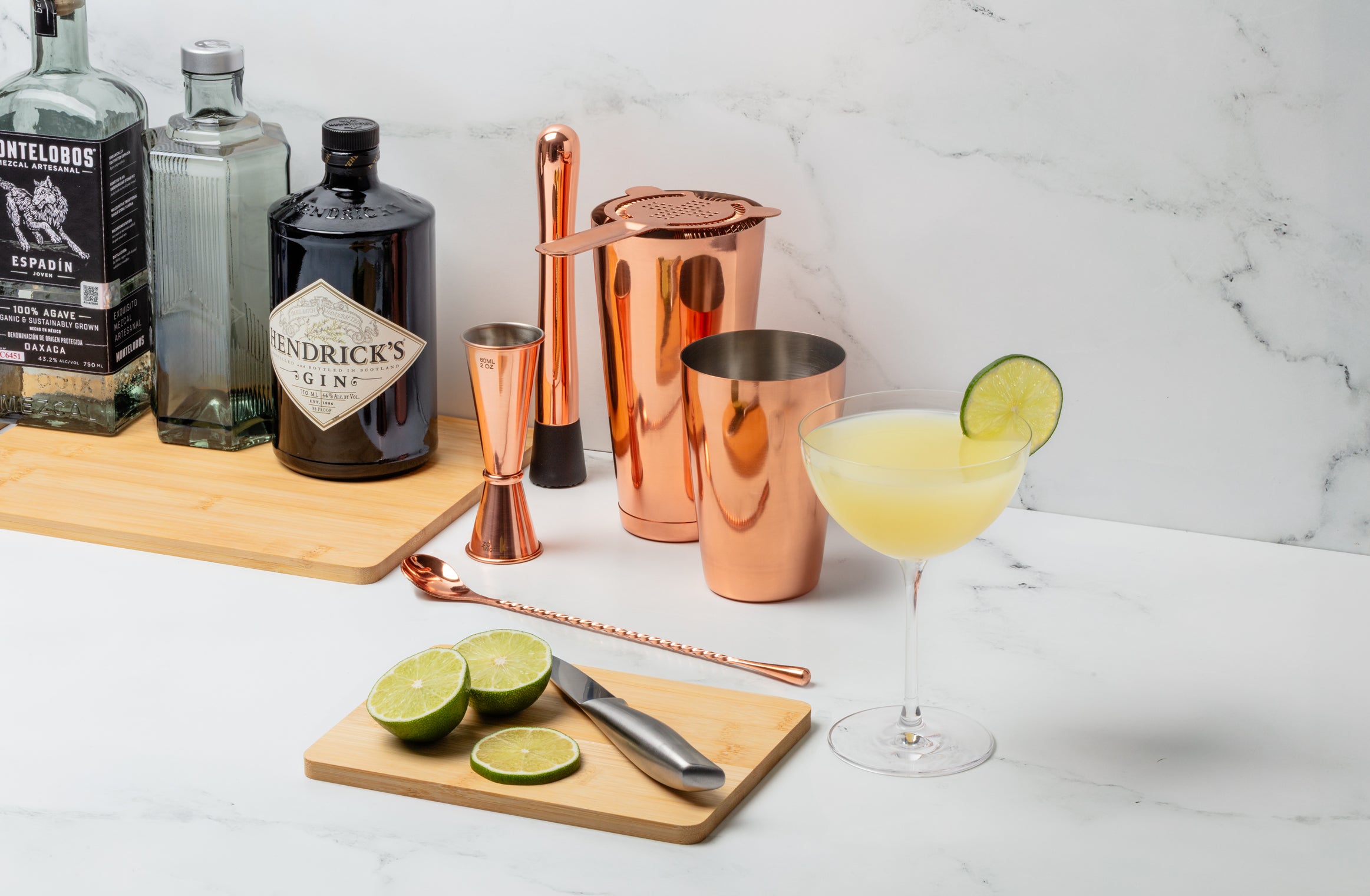 Cocktail setup with bottles, shakers, and a cocktail on a marble surface