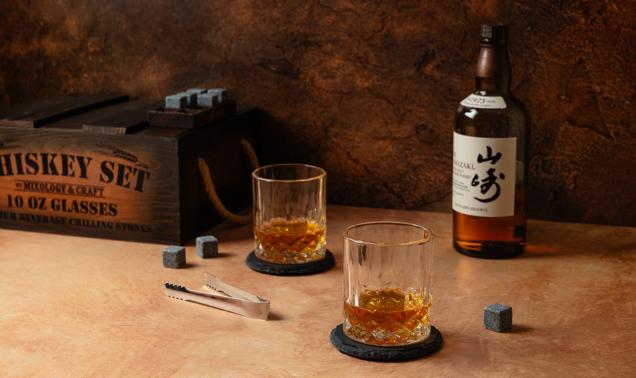 Two glasses of whiskey with a bottle and wooden crate on a wooden surface.