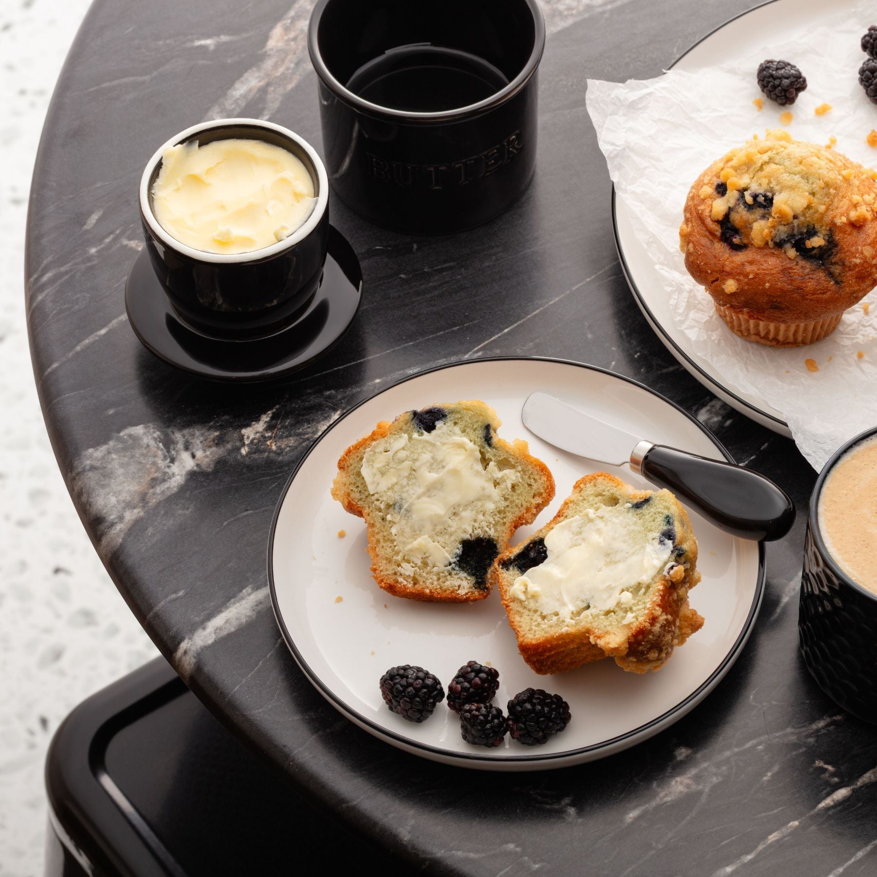 Breakfast setting with toast, blackberries, Zulay Kitchen butter crock set, and coffee on a marble surface.