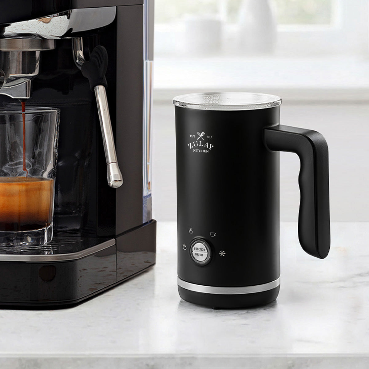 Black milk frother next to a coffee machine on a marble countertop
