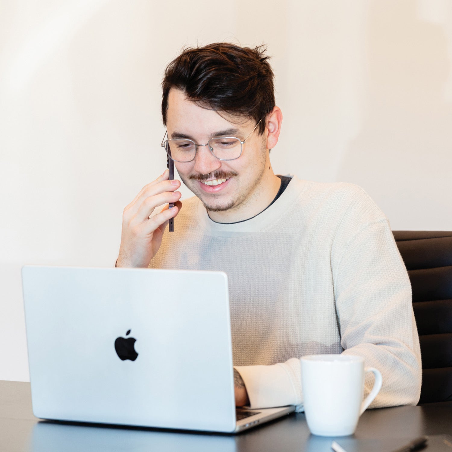 A man talking through his phone while facing into his laptop.