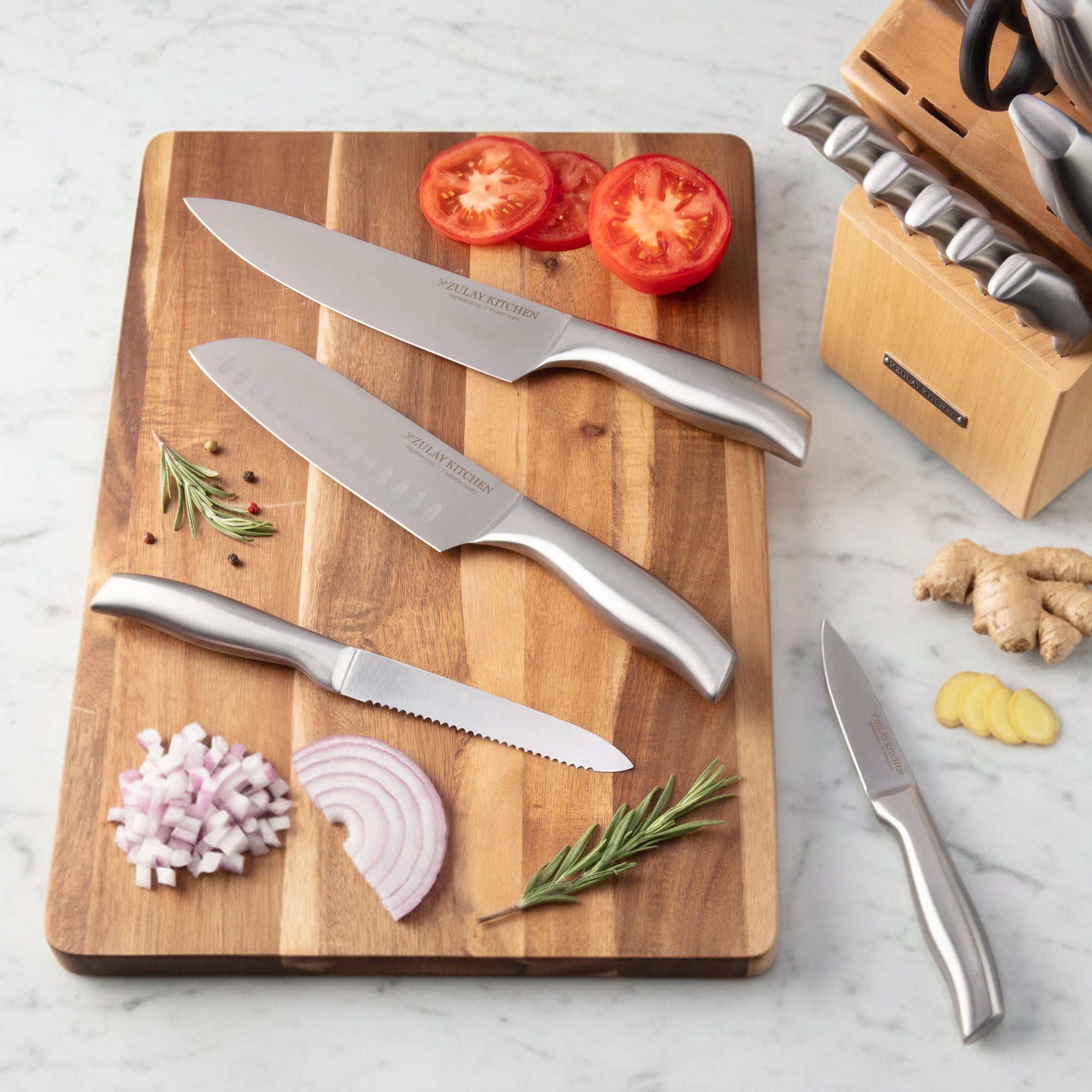 Set of knives on a wooden cutting board with vegetables on a marble surface