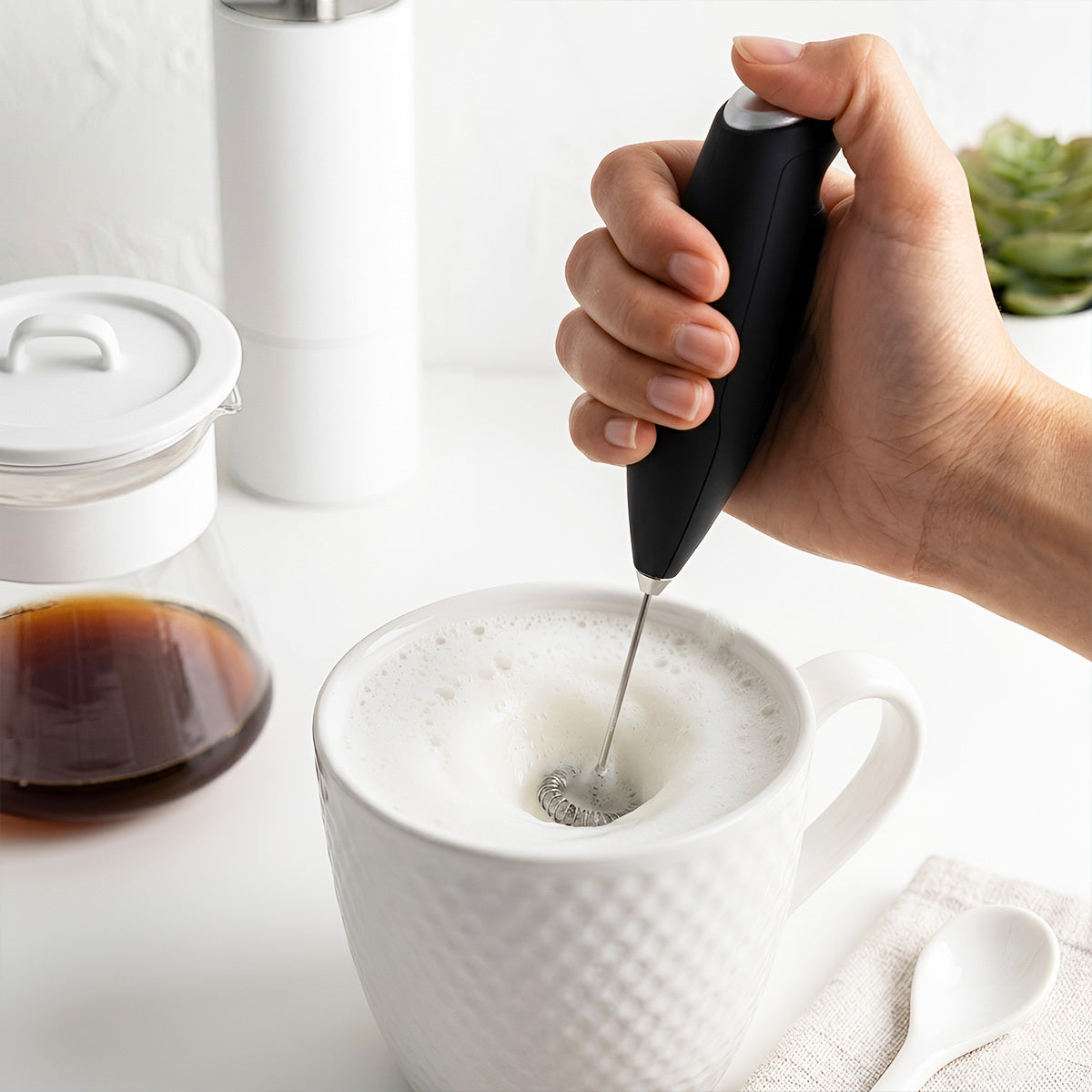Hand using a milk frother to create foam in a white mug on a light surface.