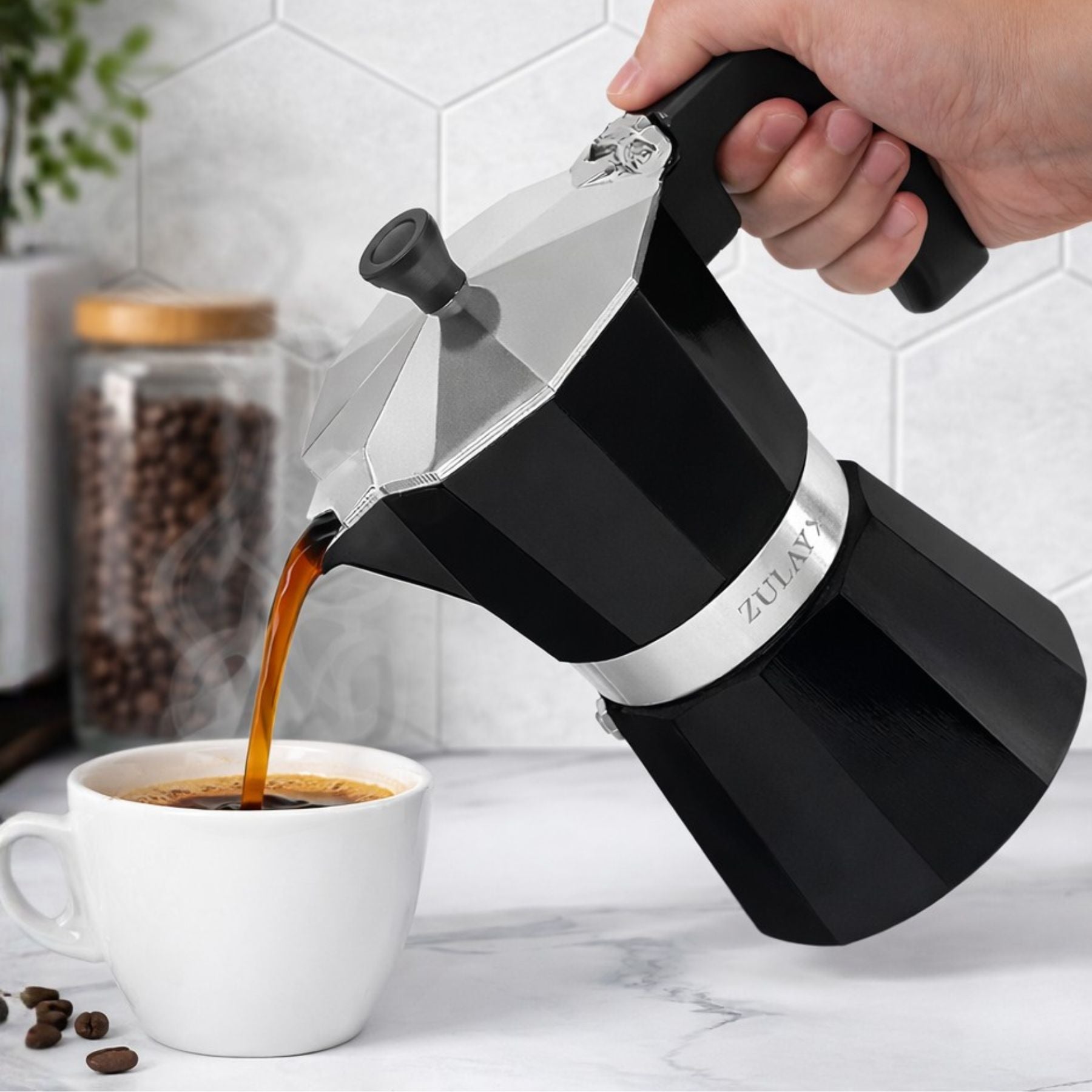 Person pouring coffee from a Zulay coffee press into a white mug on a kitchen counter.