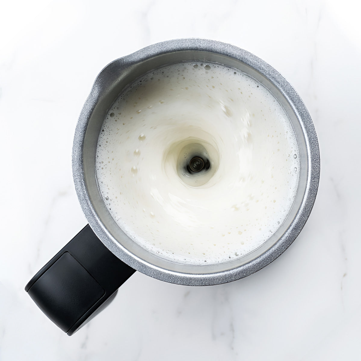 Foamy milk in a Zulay Kitchen black automatic milk frother on a marble surface
