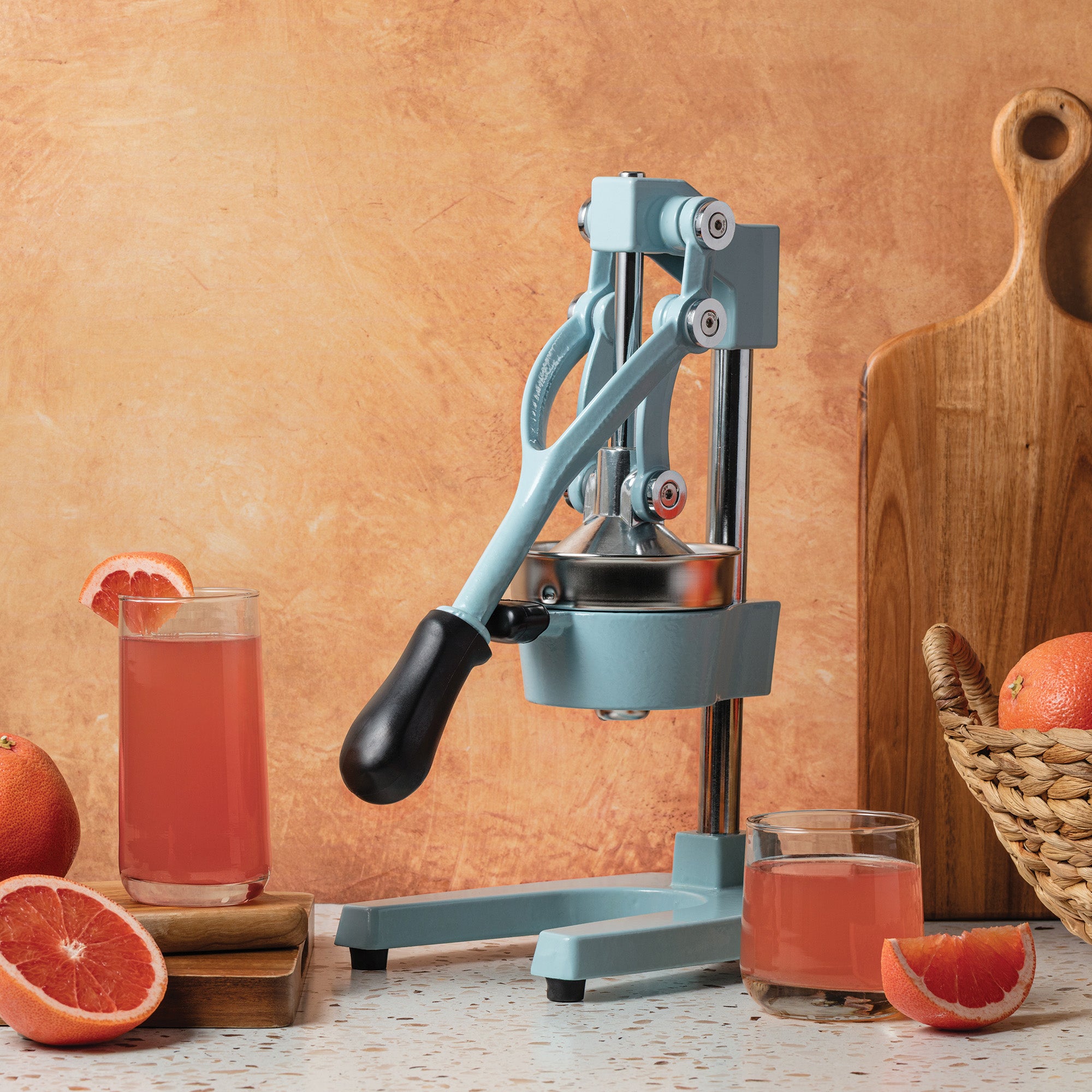 Manual juicer with glasses of juice and oranges on a wooden surface