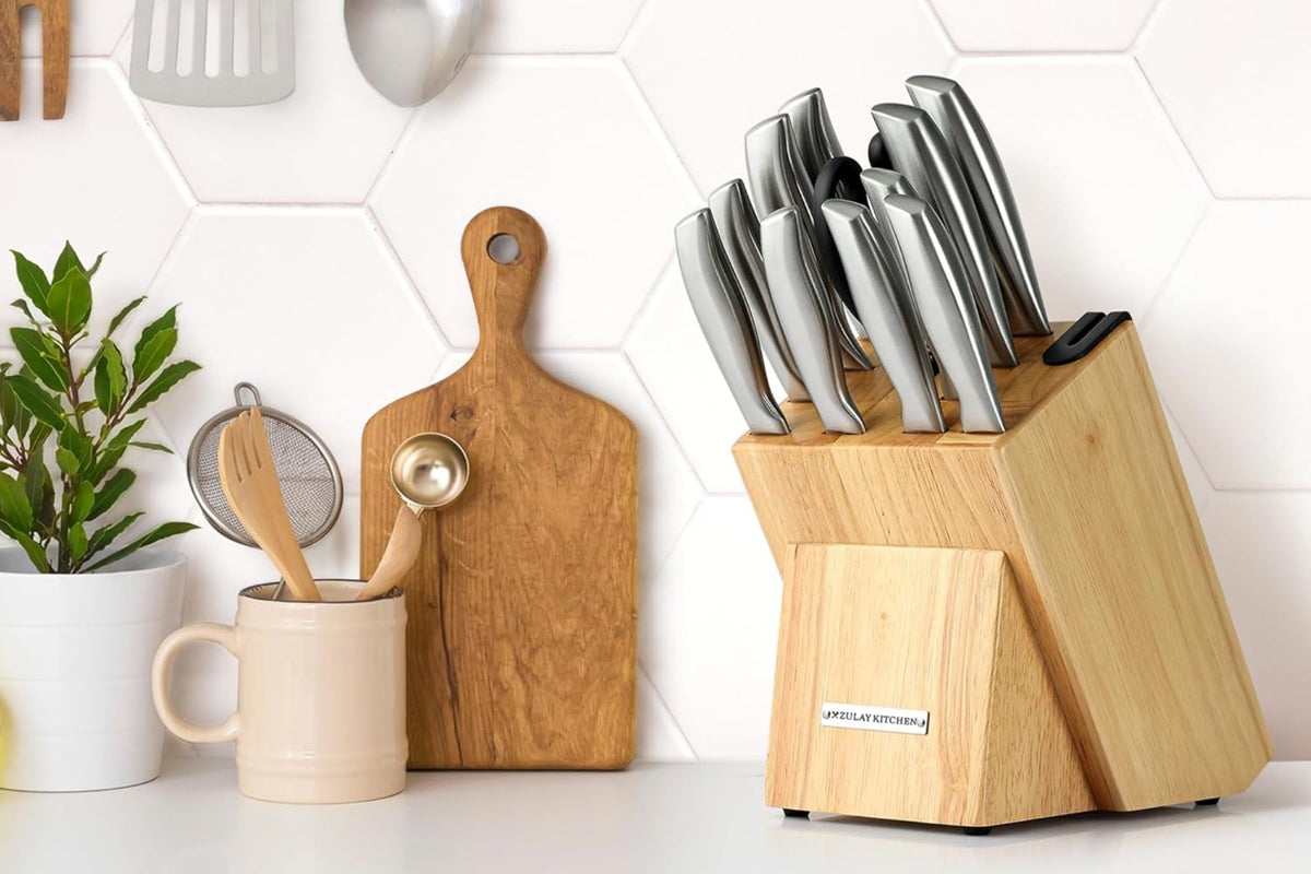 Zulay Kitchen Knife block with knives, wooden cutting board, and kitchen utensils on a white countertop.