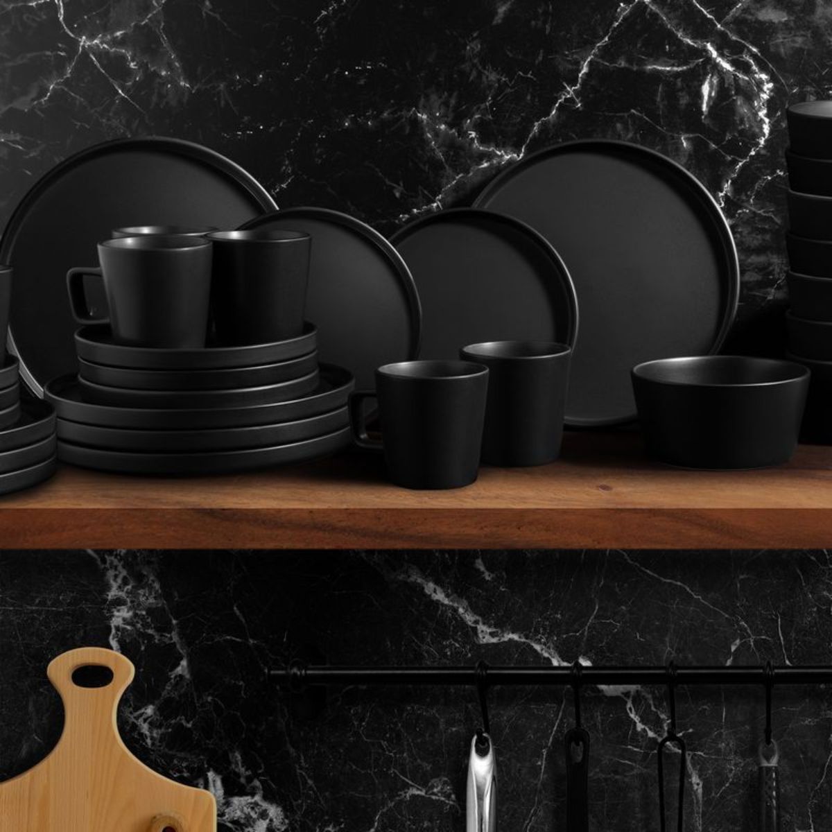 Black ceramic dinnerware set on a wooden shelf with a marble wall background