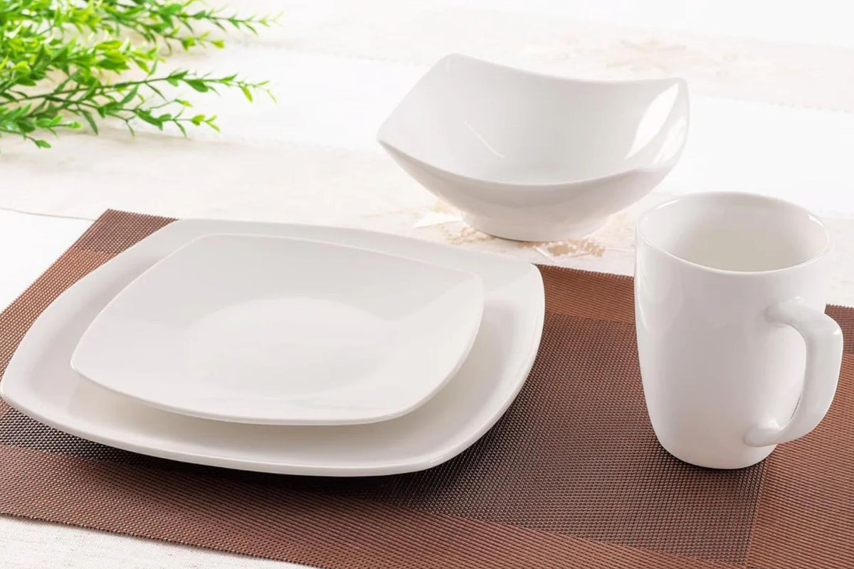White Luna porcelain dinnerware set on a brown placemat with a green plant in the background