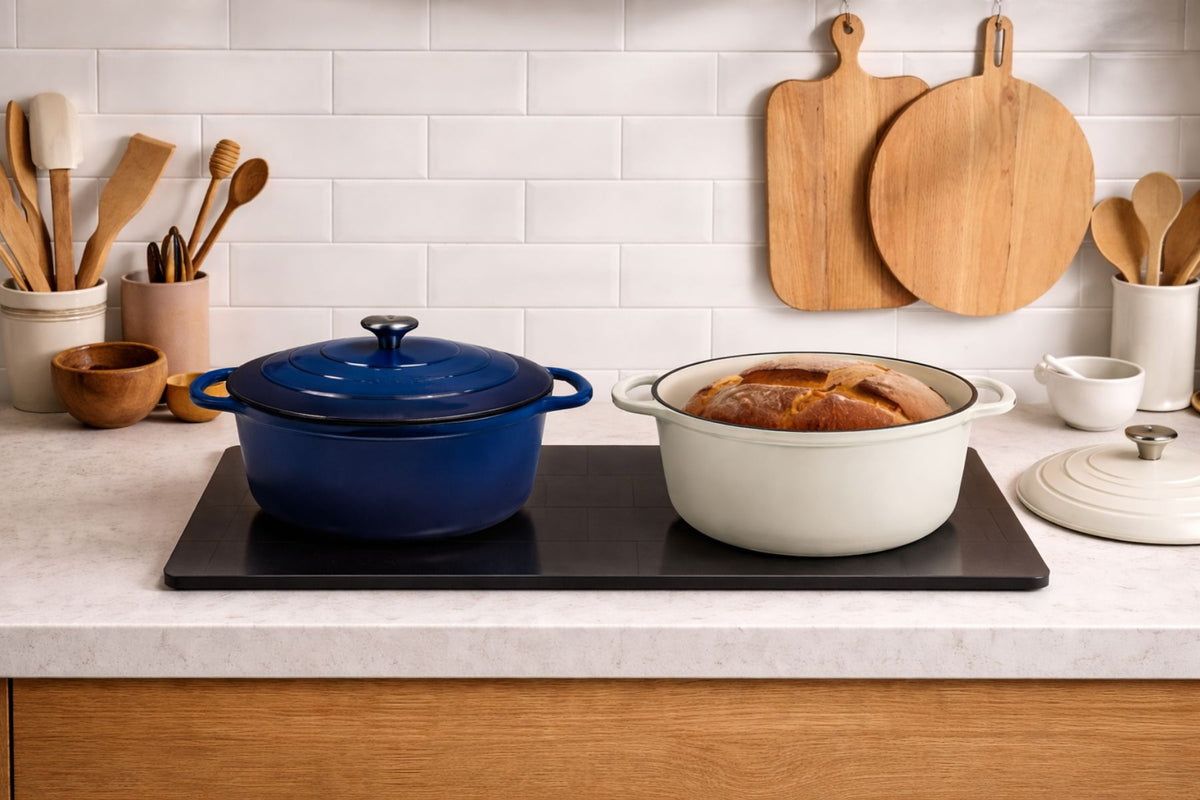 Two cookware items on a kitchen counter with wooden cutting boards and utensils in the background.