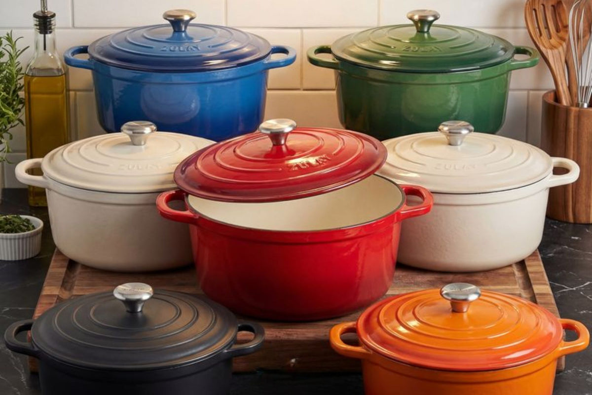 Set of colorful cast iron cookware on a wooden board with a kitchen background.