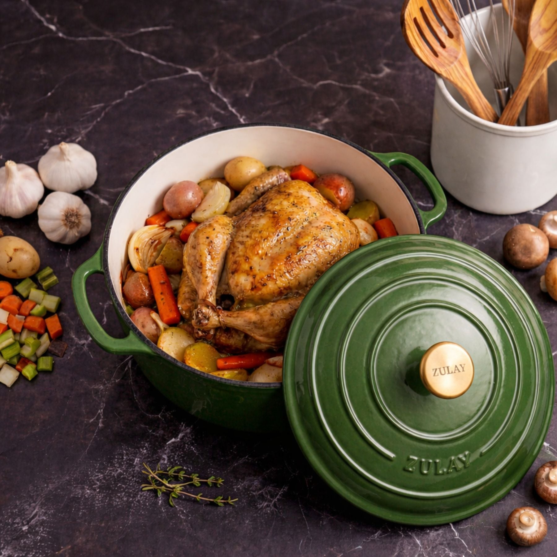 Roasted chicken with vegetables in a green Staub cocotte on a dark surface.