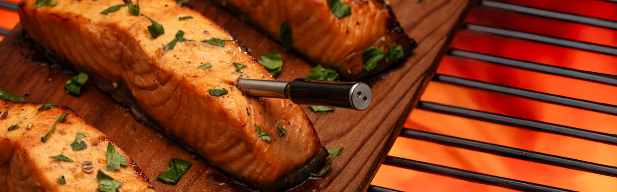 Grilled salmon fillets on a wooden board with a grill in the background