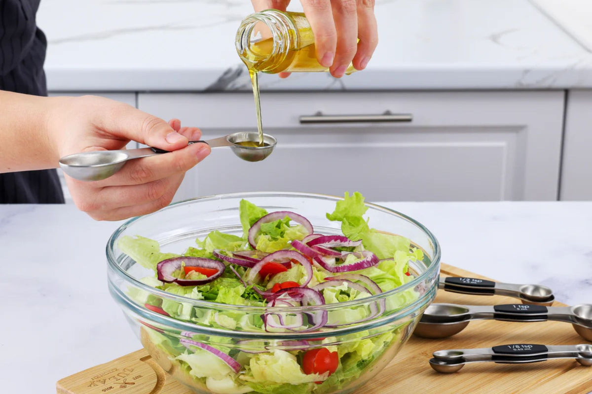 Person drizzling olive oil over a salad in a kitchen setting