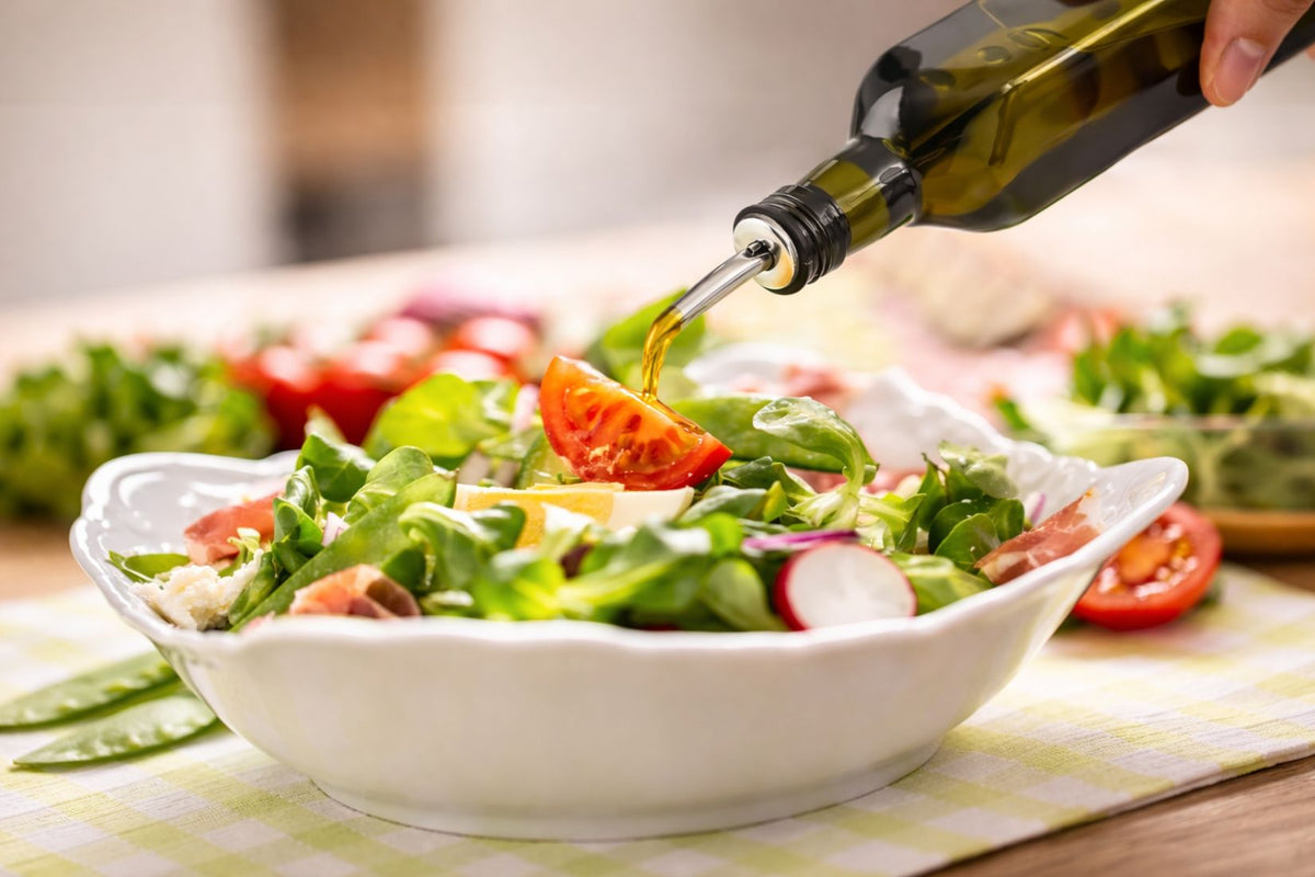 Person pouring olive oil over a salad in a white bowl on a checkered tablecloth.