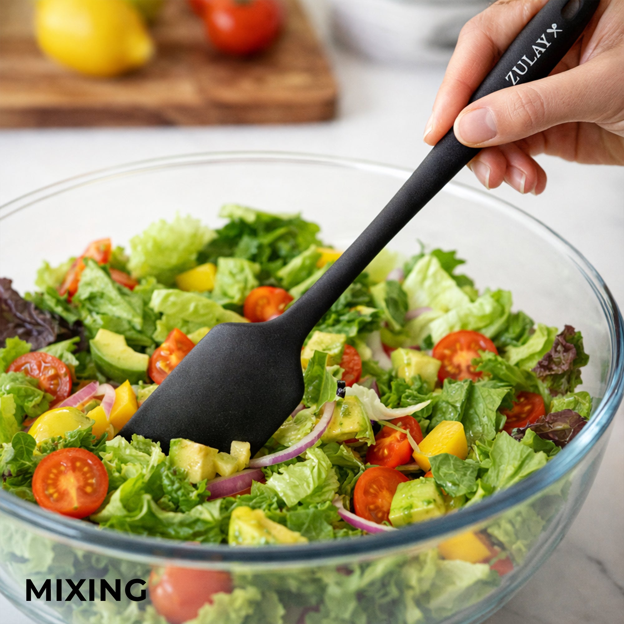 Person using a black Zulay kitchen spatula to mix a salad in a glass bowl.