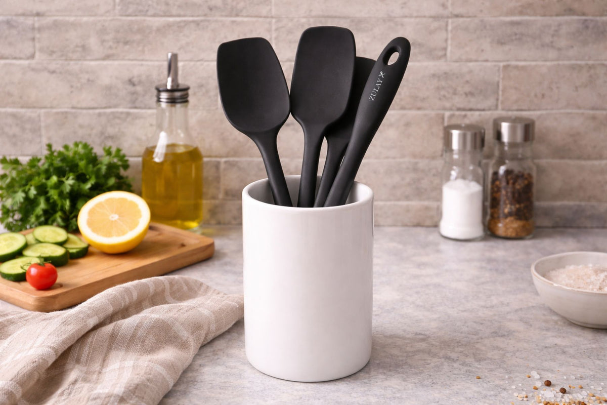 Black Zulay kitchen silicone spatula in a white container on a kitchen counter with ingredients in the background.