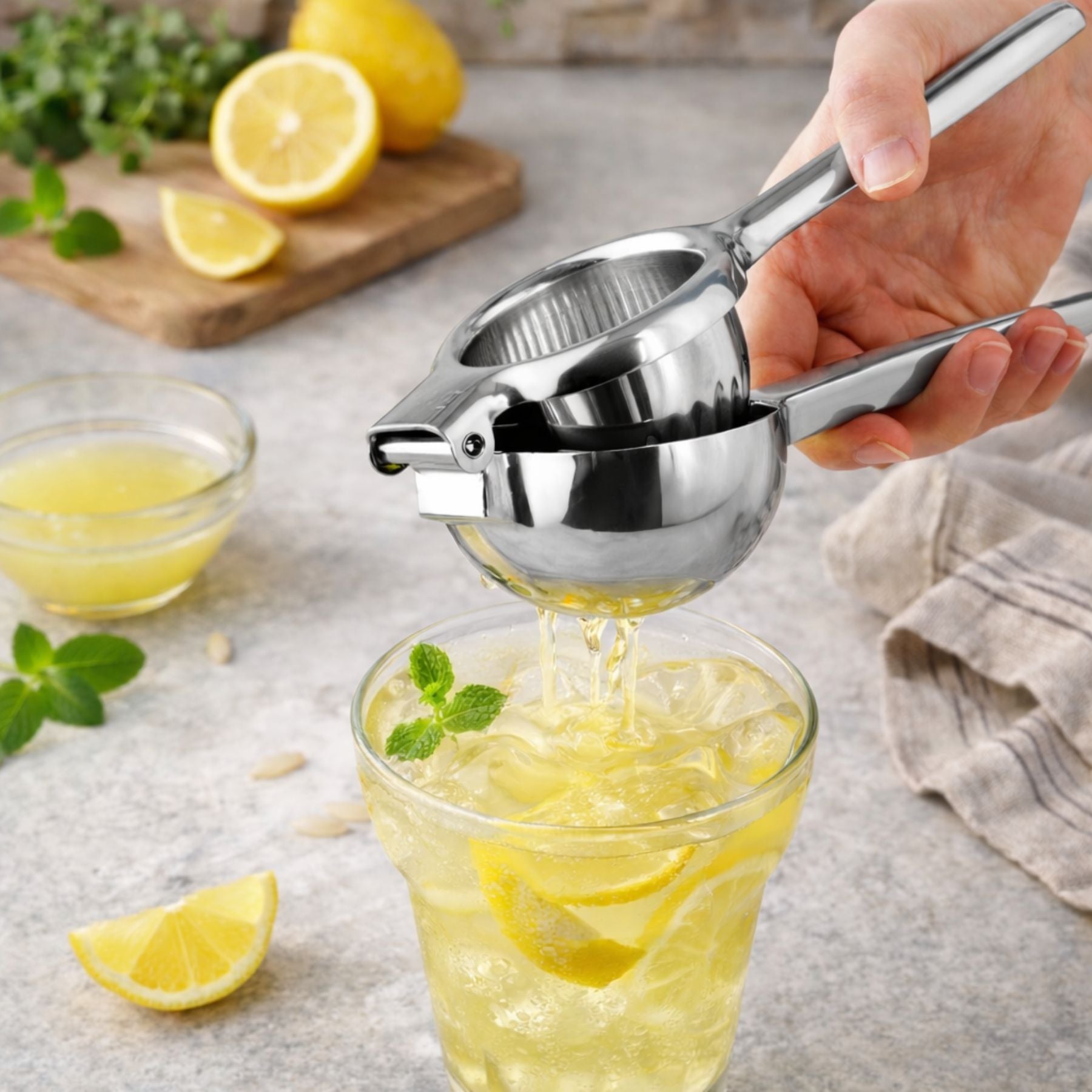 Person using a Zulay Kitchen Stainless Steel Lemon Squeezer to extract juice into a glass with lemon slices.