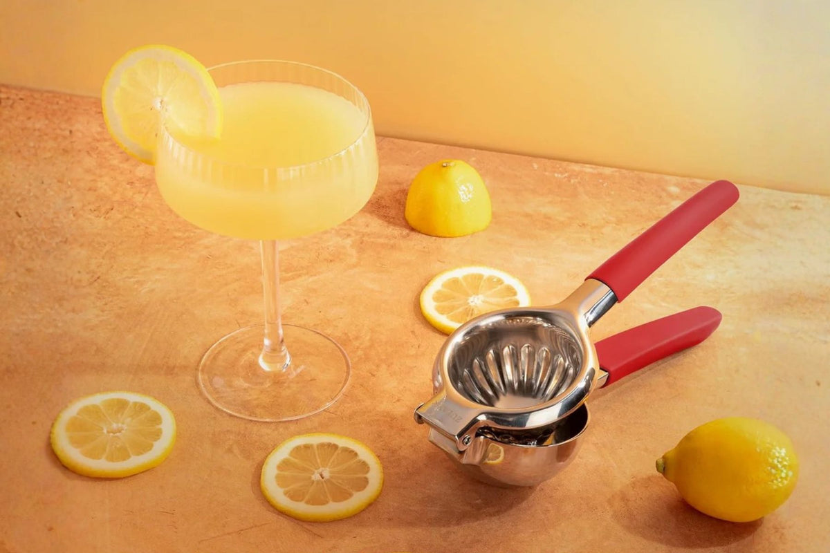 Cocktail with lemon slices and a Zulay Kitchen Stainless Steel Lemon Squeezer on a wooden surface