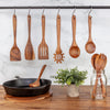 Wooden kitchen utensils hanging on a rack with a marble wall and wooden table in the background.