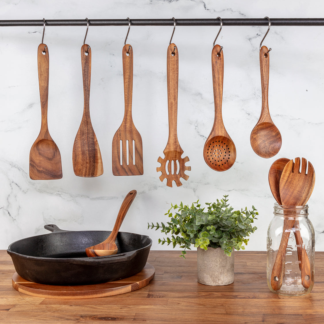 Wooden kitchen utensils hanging on a rack with a marble wall and wooden table in the background.