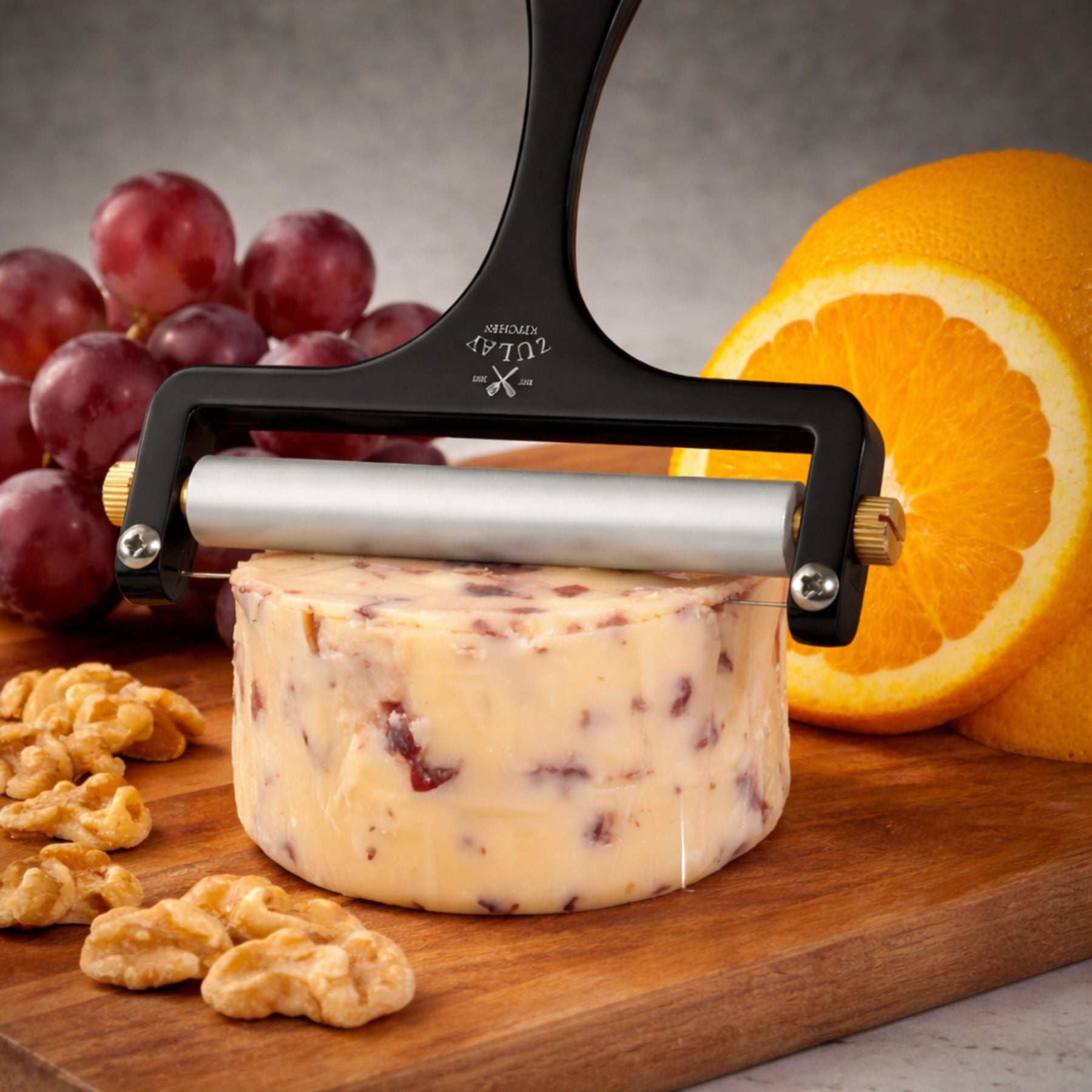 The Zulay Kitchen Wire Cheese Slicer cutting into a block of cheese with grapes, oranges, and walnuts on a wooden board.