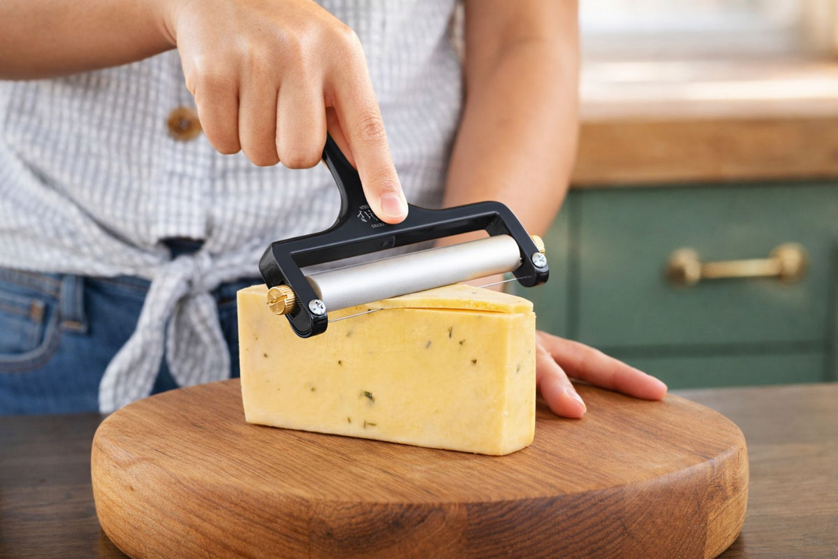 Person using the Zulay Kitchen Wire Cheese Slicer on a block of cheese on a wooden cutting board.