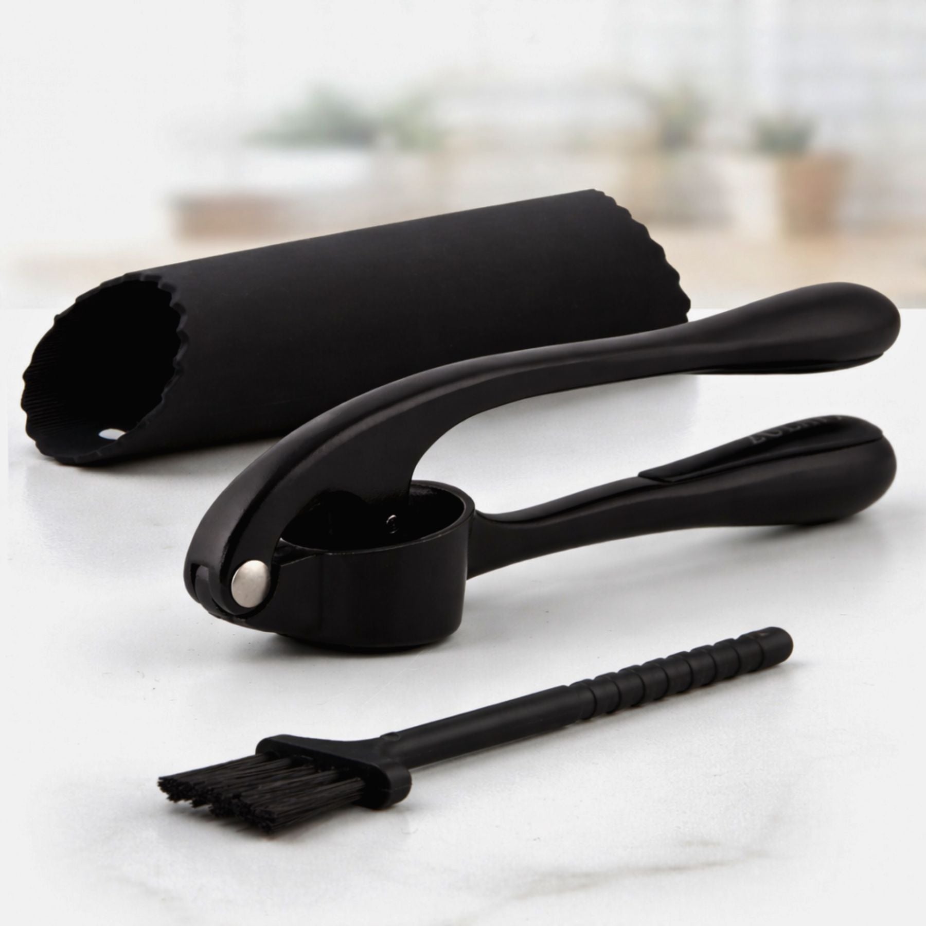 Set of black Zuki Garlic Press Set including a roller, measuring spoon, and brush on a light surface.