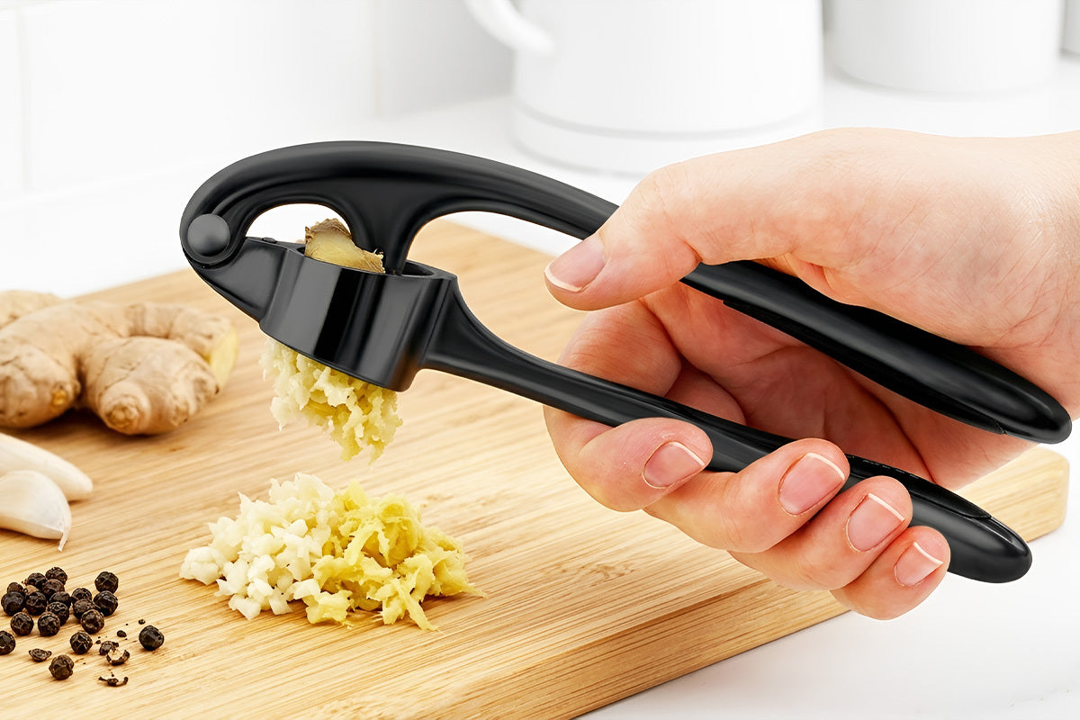 Black Zuki Garlic Press Set being used on a wooden cutting board with garlic and ginger.
