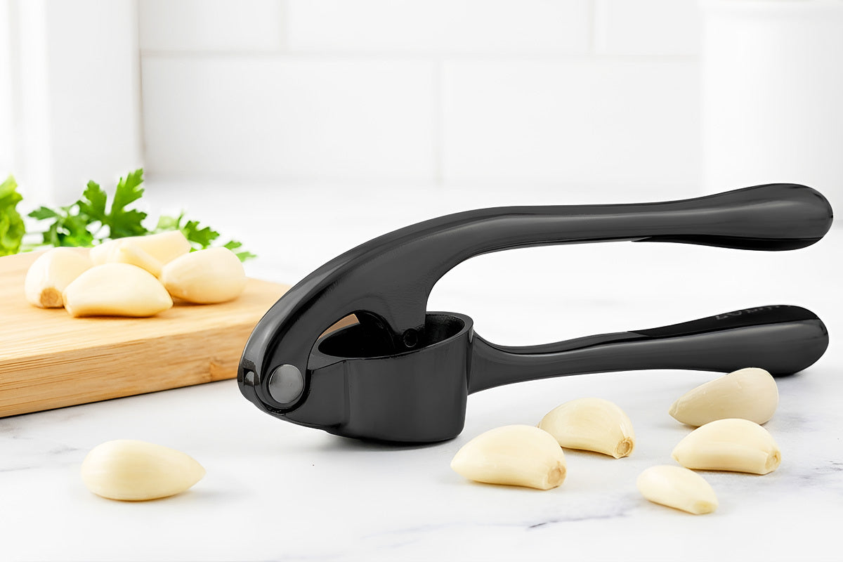 Black Zuki Garlic Press Set on a marble surface with garlic cloves and a cutting board in the background.