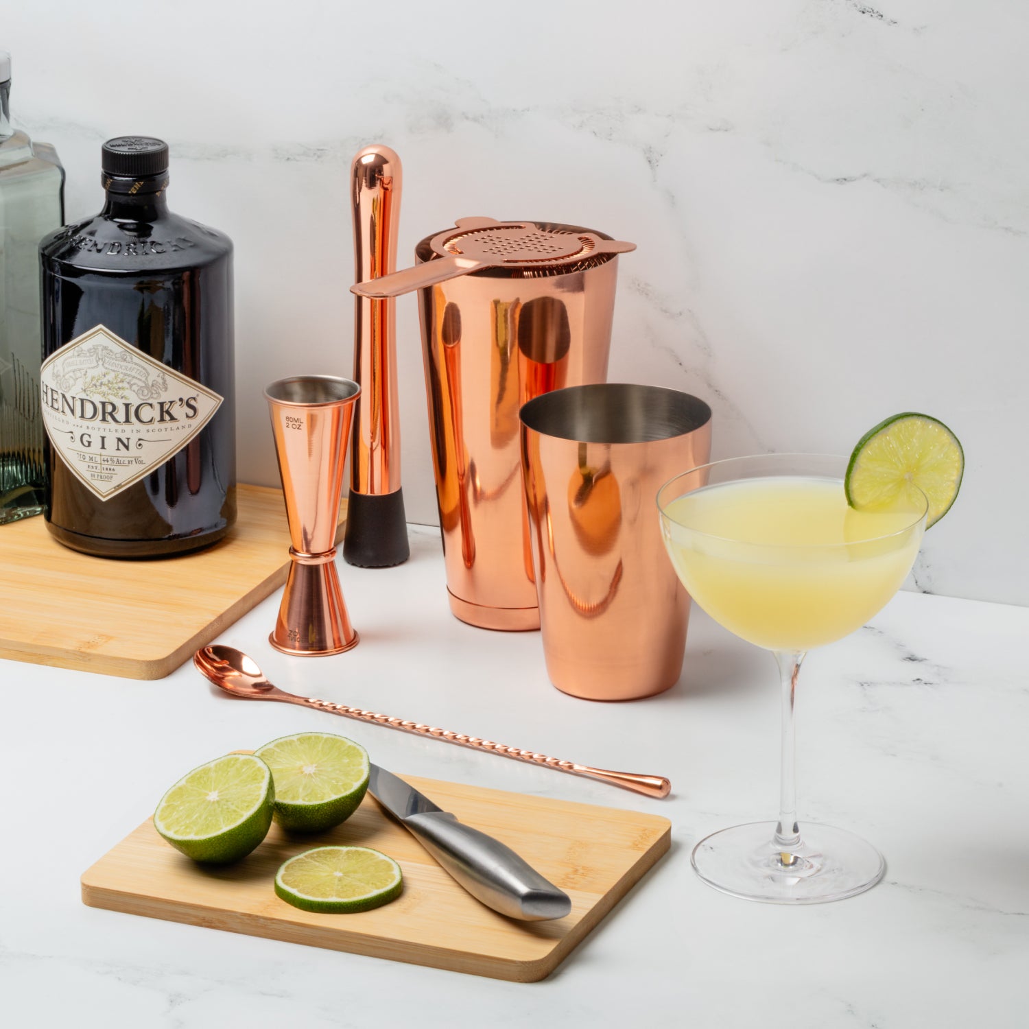Cocktail-making setup with Hendrick's gin, copper bar tools, and a cocktail garnished with a lime.